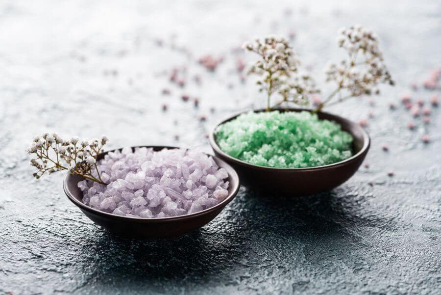 fioletowa i zielona sól morska w miseczkach, ozdobione kwiatami