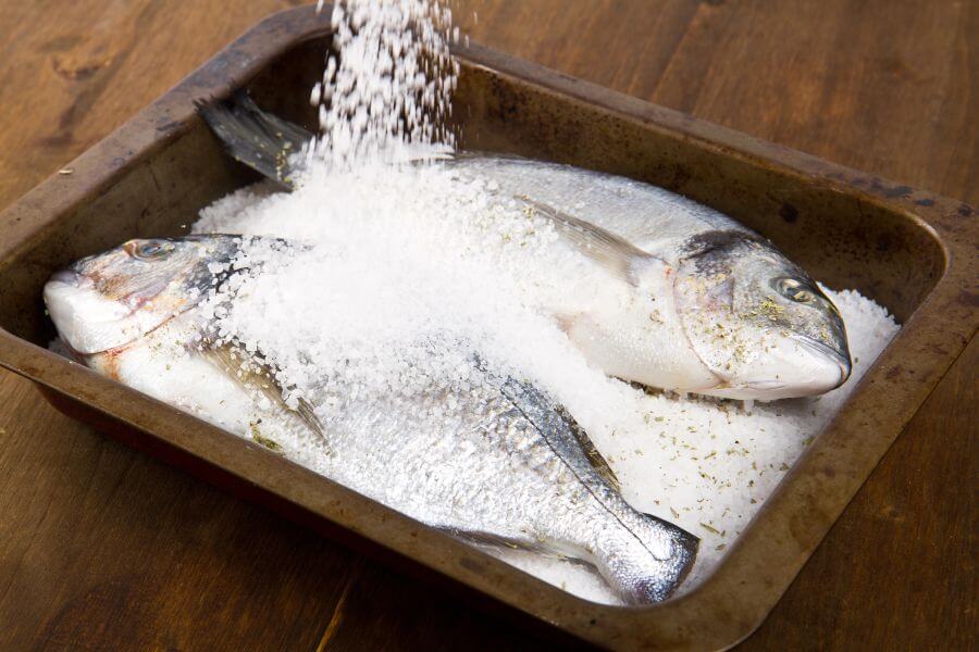 ryby na tacce do pieczenia posypywane solą morską